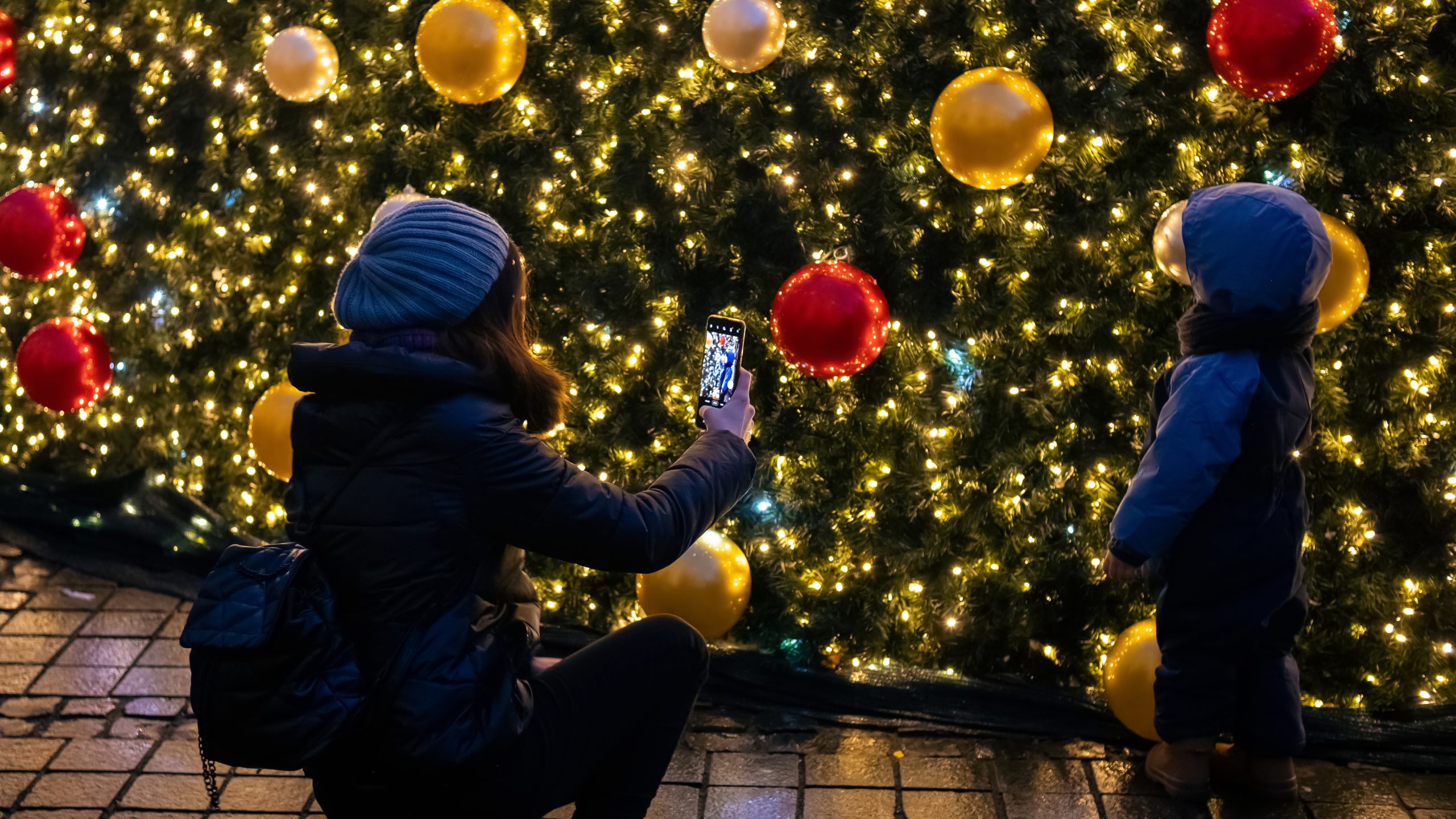 A mother taking a photo of her child in front of a Christmas tree. Winter decorations